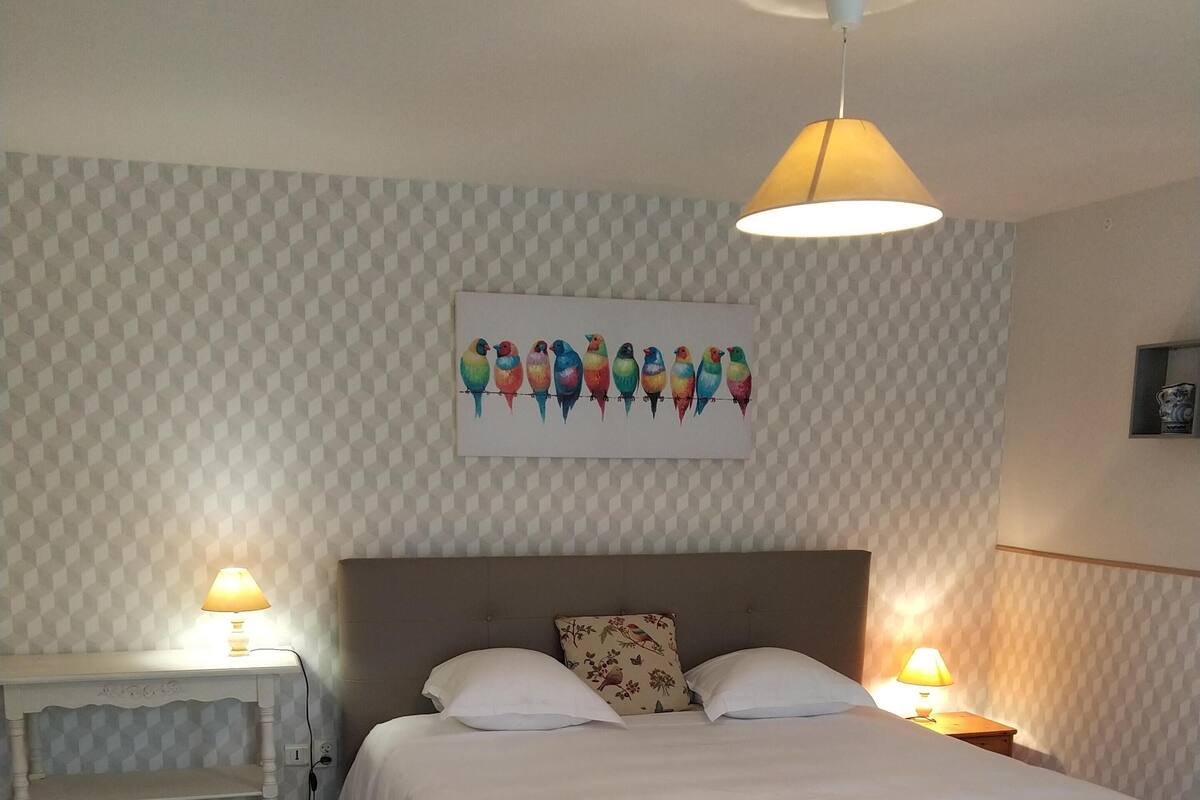 A bedroom with a bed, two bedside tables, a wall-mounted lamp, and a wall art piece.