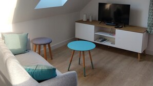 Una sala de estar moderna con techo inclinado, un sofá, una mesa de centro, un televisor y una pequeña mesita auxiliar.