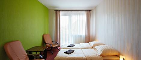 Habitación de hotel con dos camas, pared verde, ventana con cortinas y una pequeña mesa.