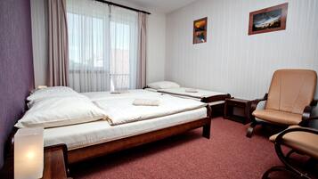 A hotel room with a large bed, a smaller bed, a chair, a bedside table, and a lamp.