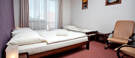 A hotel room with a large bed, a smaller bed, a chair, a bedside table, and a lamp.