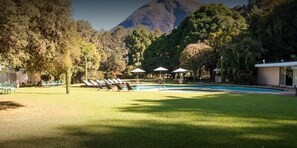 A pool area with lounge chairs and umbrellas, surrounded by trees and a mountain in the background. - Altenhaus Pousada (Petrópolis)