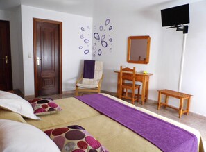 Un dormitorio con cama, escritorio, silla, televisor y puerta.