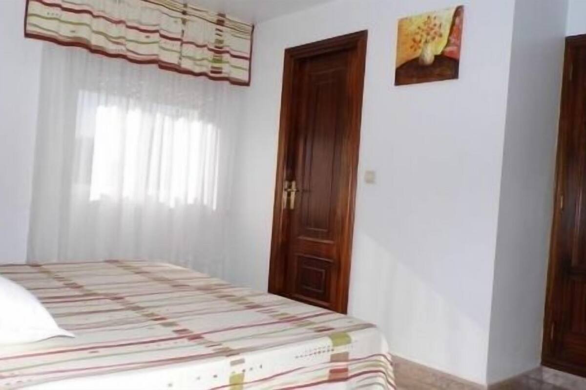 A bedroom with a bed, a window with curtains, and two doors.