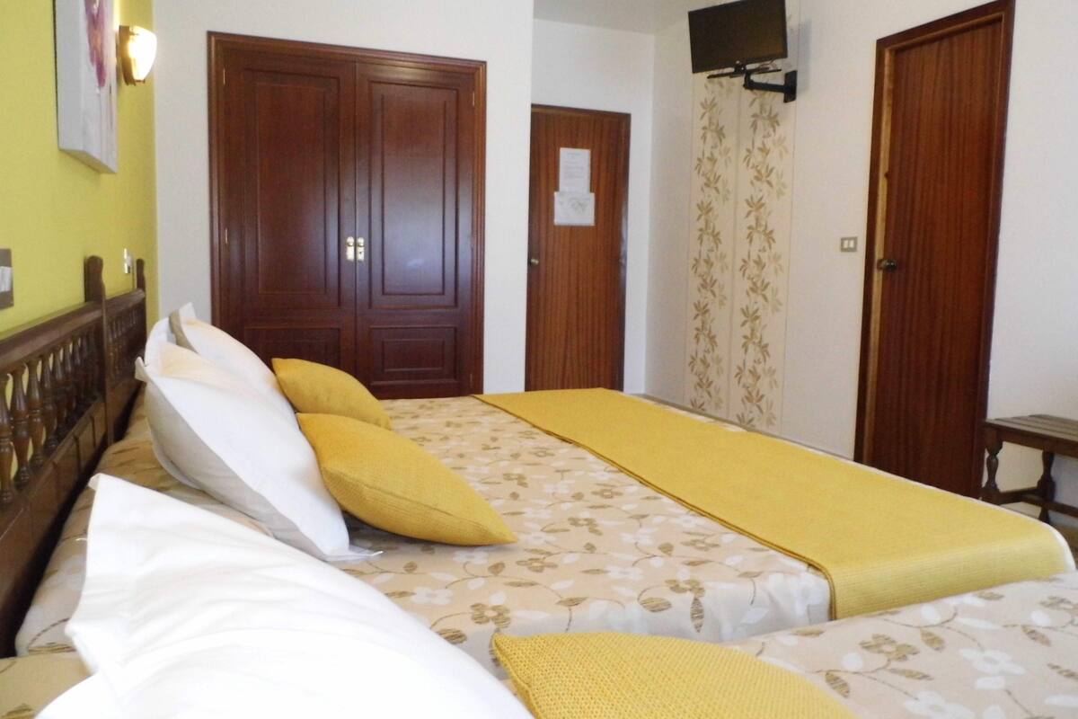 A hotel room with a double bed, a wooden wardrobe, a television mounted on the wall, and a door with a floral curtain.