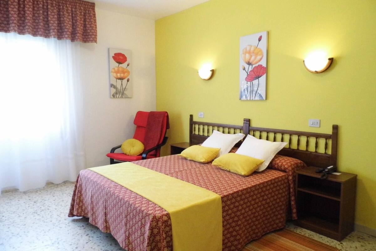 A bedroom with a bed, a chair, a nightstand, and wall art.