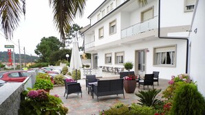 A hotel patio with outdoor seating, potted plants, and a view of the street. - Hotel Arboleda (Sanxenxo)