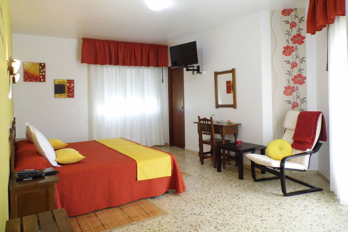 A hotel room with a bed, a desk, a chair, a TV, and a window with curtains.