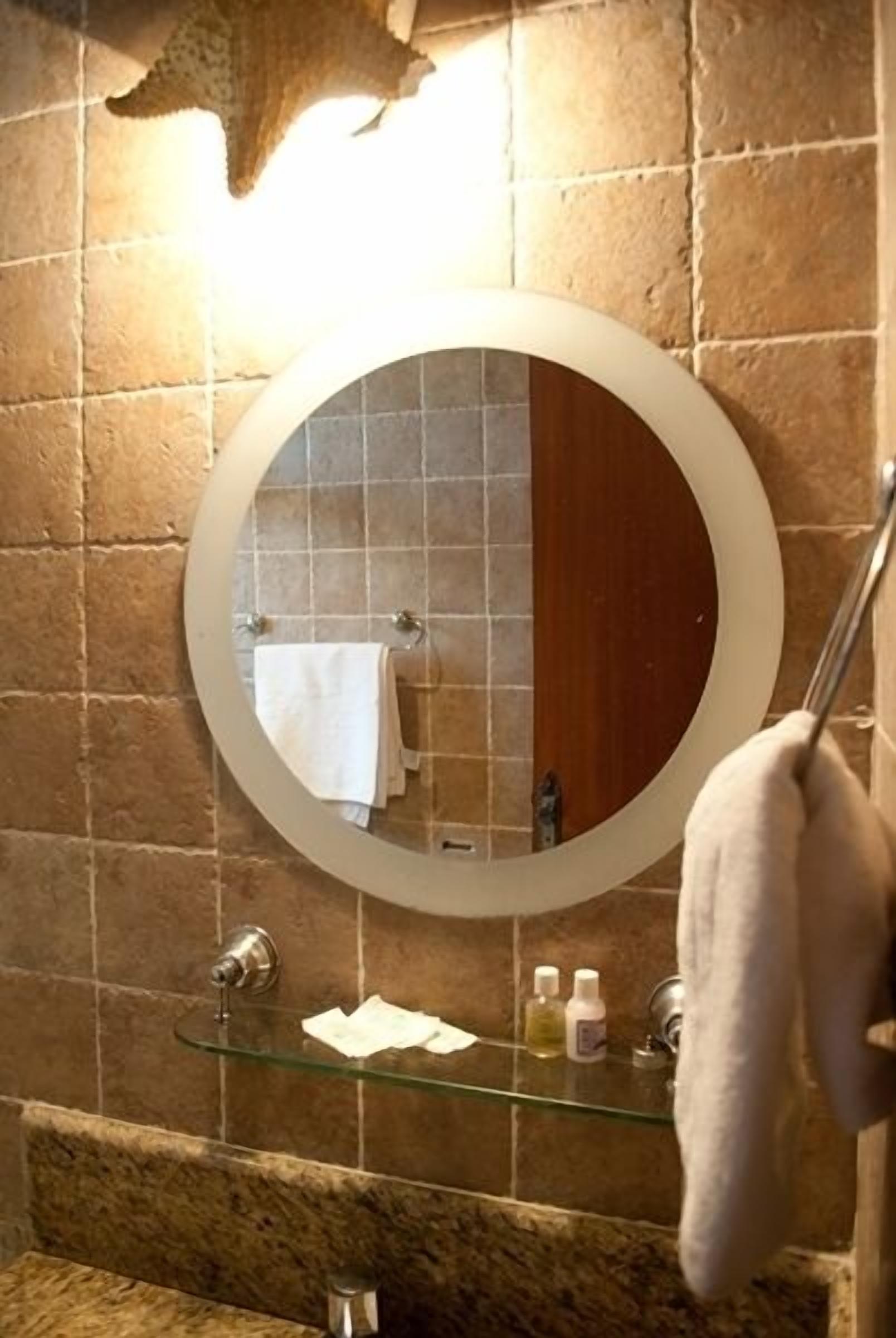 Un baño con un espejo redondo, un estante de vidrio y un perchero para toallas.