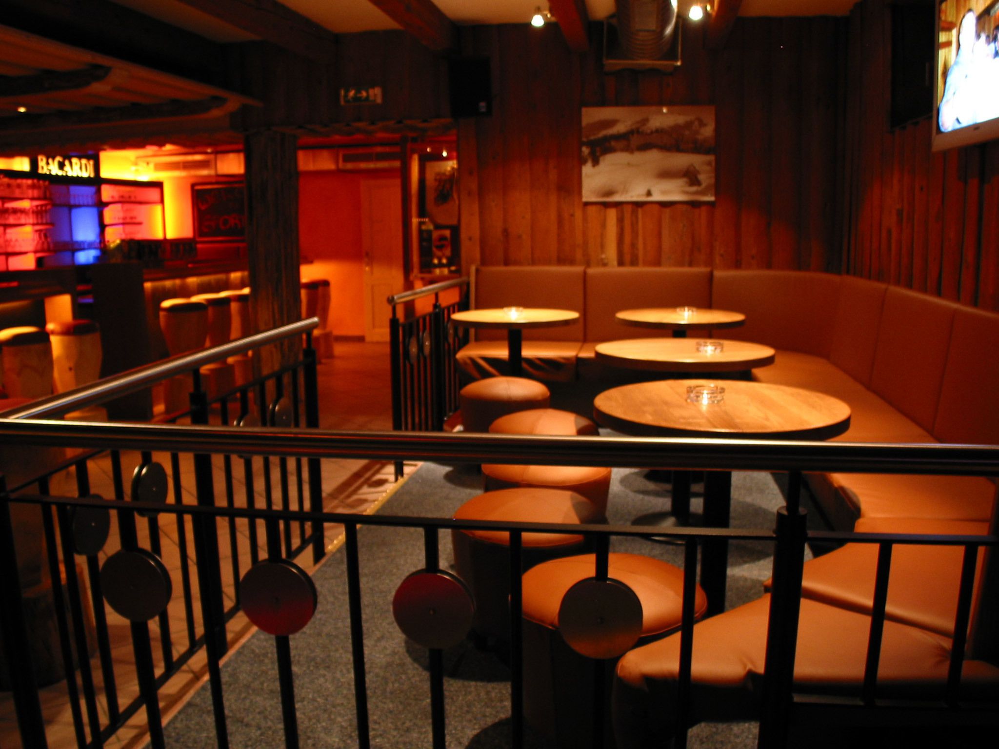 A dimly lit bar area with wooden booths and round tables.