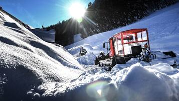 A snow grooming machine on a snowy slope with a clear sky.