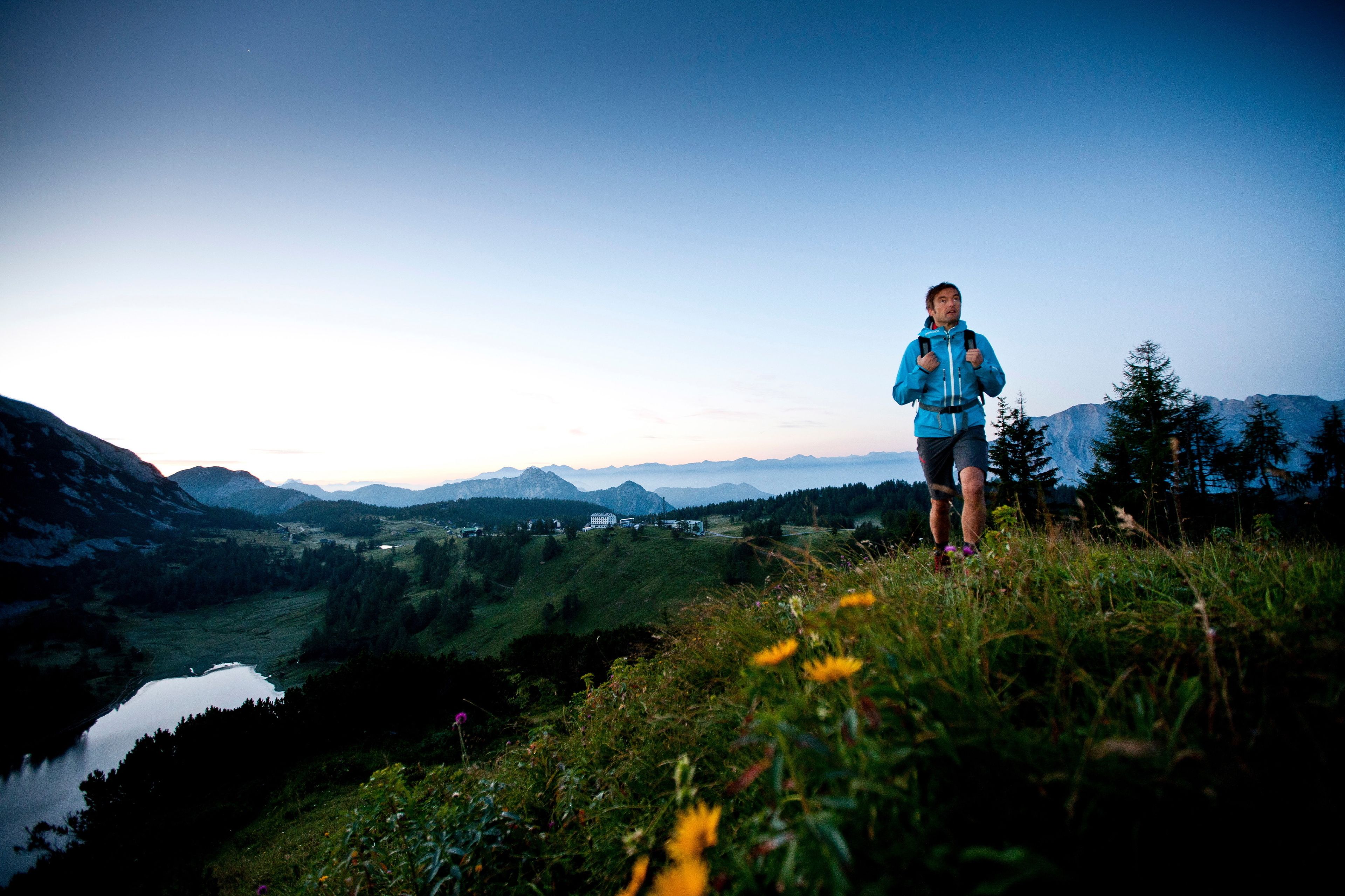 A person standing on a grassy hill overlooking a valley with mountains in the distance.