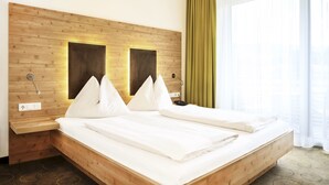 Una cama grande con cabecera de madera, dos mesitas de noche y una ventana con cortinas.