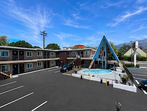 A motel with a swimming pool, multiple parking spaces, and a mountain backdrop.