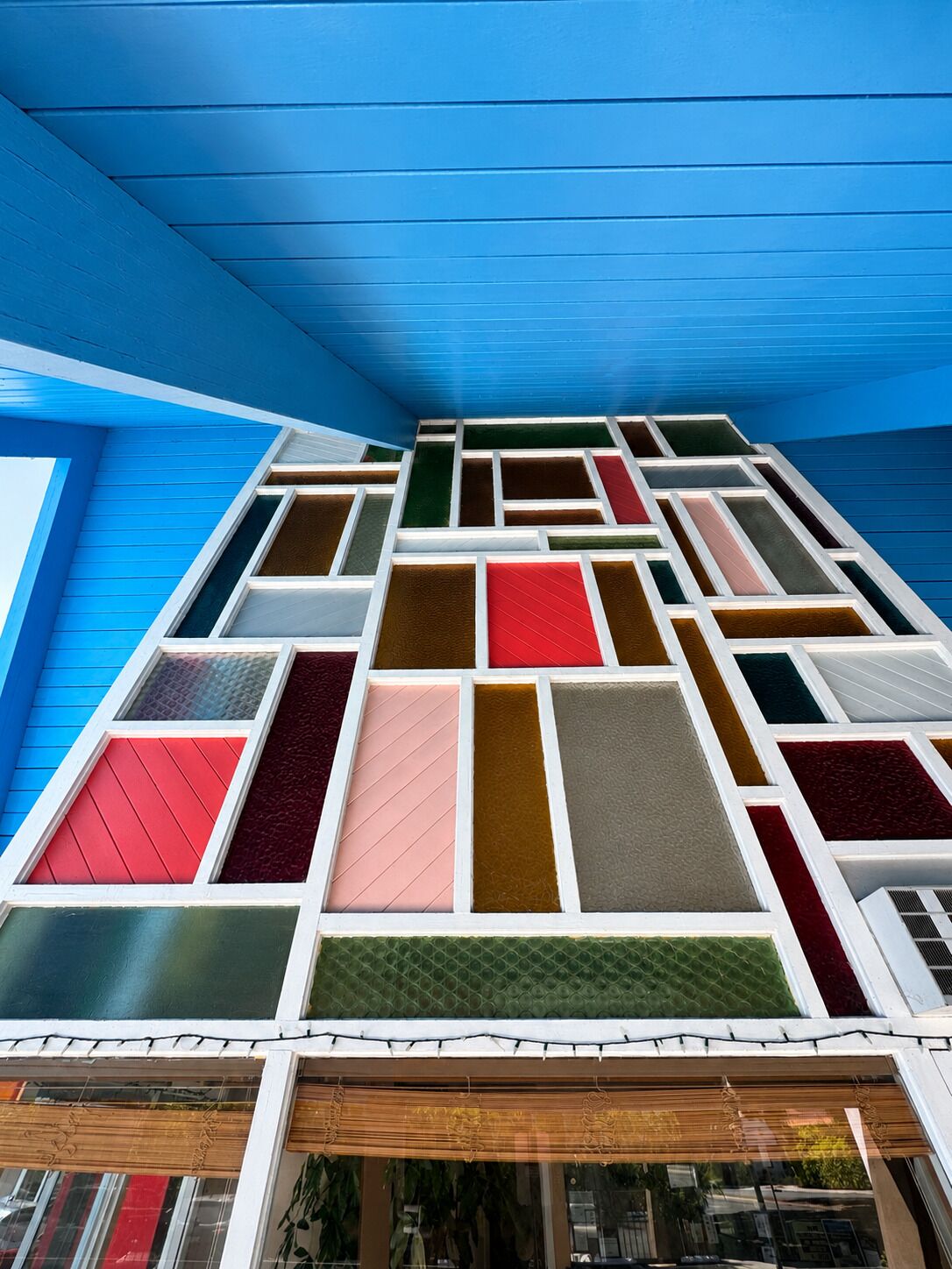 Een meerhoog gebouw met een blauwe gevel en een reeks ramen met verschillende gekleurde glaspanelen.
