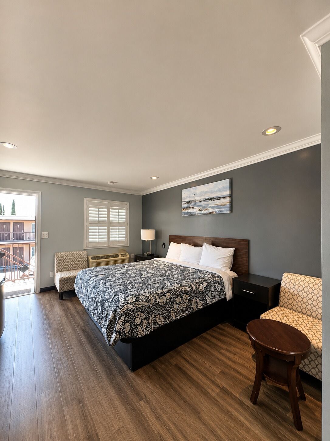A bedroom with a bed, bedside table, chair, and a view of the outside.