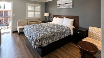 A bedroom with a bed, bedside table, chair, and a view of the outside.