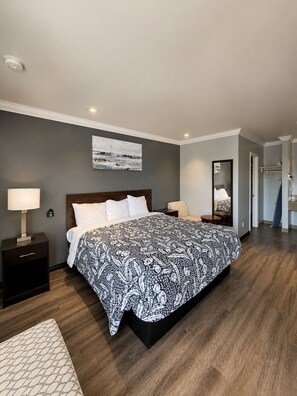 A bedroom with a large bed, a nightstand, a bedside lamp, and a painting on the wall. - La Casa Inn (Pasadena)