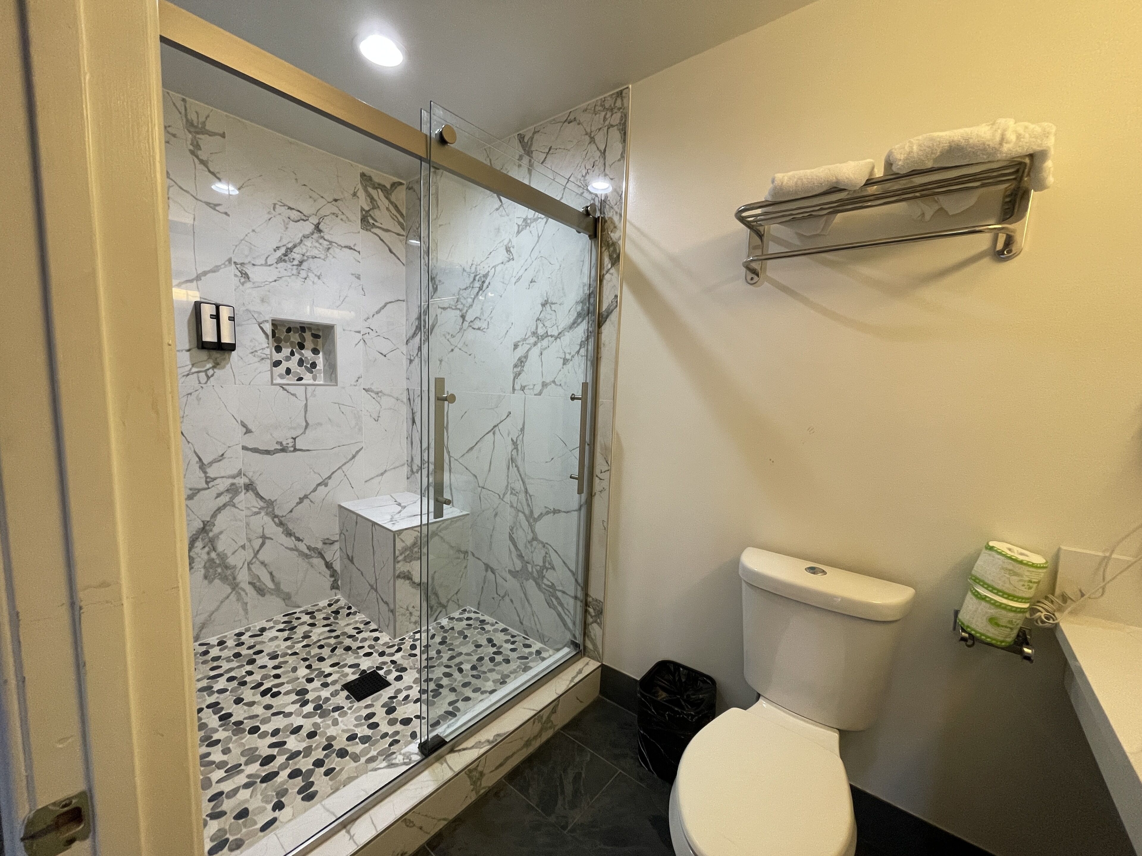 Ein Badezimmer mit Duschkabine, Toilette, Waschbecken und Handtuchhalter sowie einem Mülleimer.