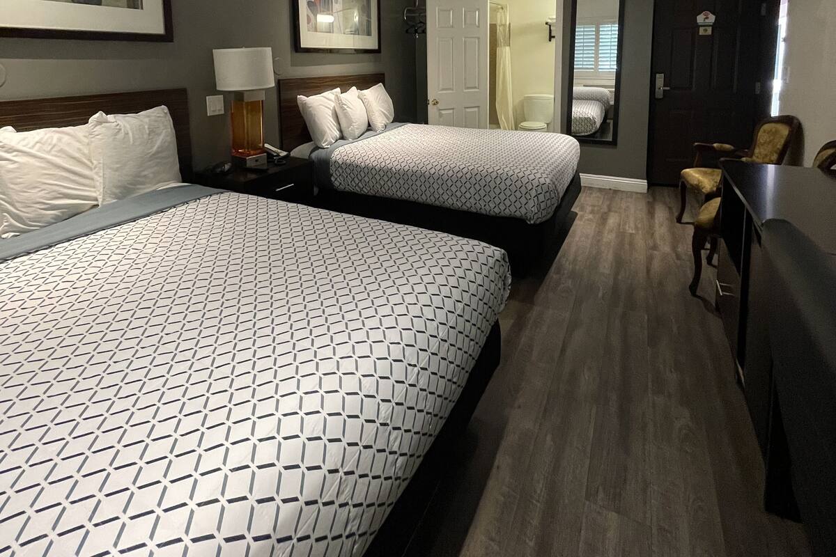 Ein Hotelzimmer mit zwei Betten, einem Schreibtisch, einem Stuhl, einem Spiegel und einer Tür zu einem Badezimmer.