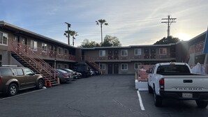 A parking lot with a white pickup truck, a black SUV, and a silver sedan. There are multiple buildings with balconies and staircases. - La Casa Inn (Pasadena)