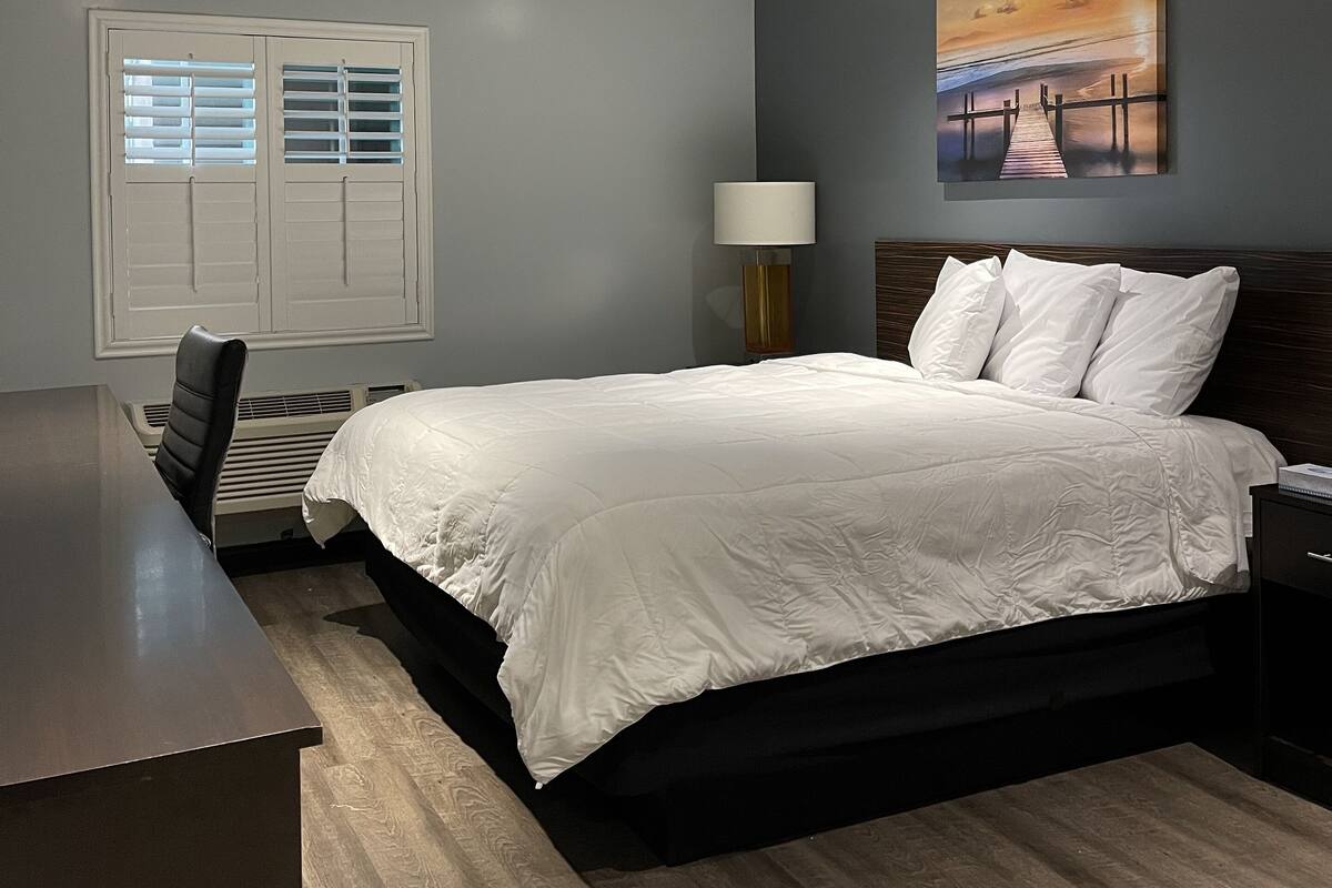 Ein Schlafzimmer mit Bett, Schreibtisch, Stuhl, Lampe und einem Gemälde an der Wand.
