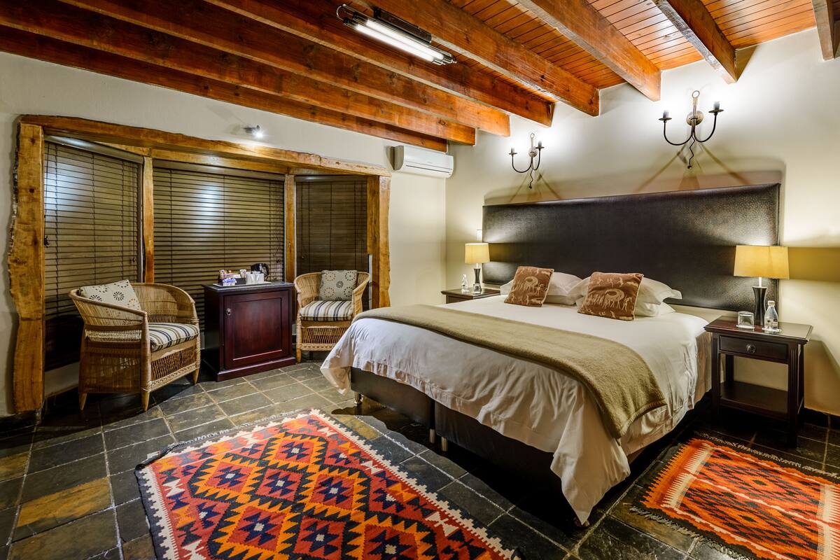 Ein Schlafzimmer mit einem großen Bett, zwei Nachttischen, einer Kommode, Korbstühlen und einem gemusterten Teppich.