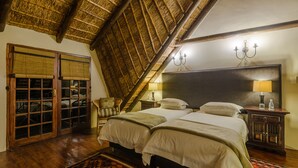 A room with two beds, a wooden floor, a thatched ceiling, and a traditional lamp. - Mongena Game Lodge (Hammanskraal)