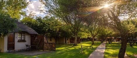 Un sendero atraviesa un jardín cuidado con árboles y un edificio con techo de paja.