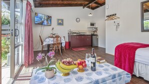 A compact room with a bed, a dining table with fruit, a kitchen area, and a TV. - Grange Motel (Auckland)