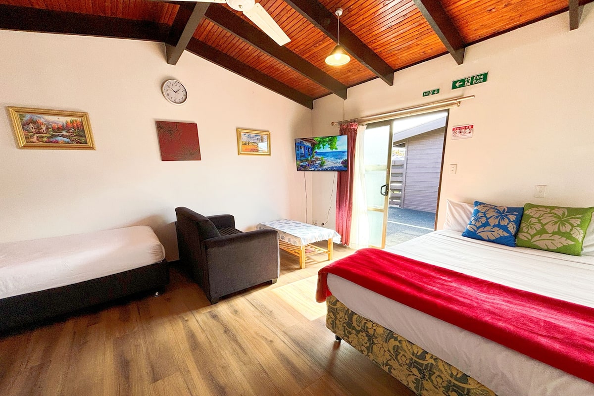 A room with two beds, a small table, a TV, and a door leading outside.