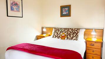 A neatly made bed with a red blanket, two bedside tables with lamps, and two framed pictures on the wall.