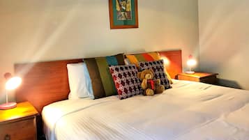 Una cama bien hecha con un oso de peluche, varias almohadas y un cuadro en la pared.