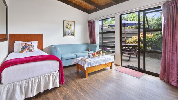 A bedroom with a bed, a sofa, a table with books, and a view of the outdoors. - Grange Motel (Auckland)