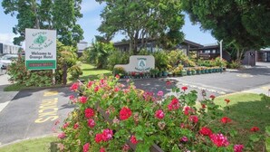 A motel entrance with a sign, a parking area, and a flower bed. - Grange Motel (Auckland)