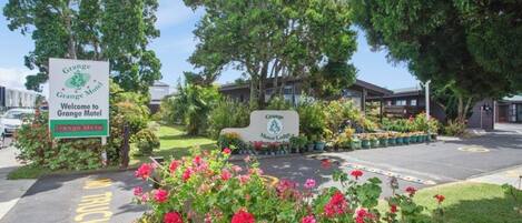 L’entrée d’un motel, avec un panneau indicateur, un espace de stationnement et un parterre de fleurs.