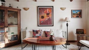 A cozy living room with a wooden dining table, a sofa with colorful cushions, a cabinet with glass doors, and two wall-mounted lamps. - Dai Nonni Hotel (Guatemala City)