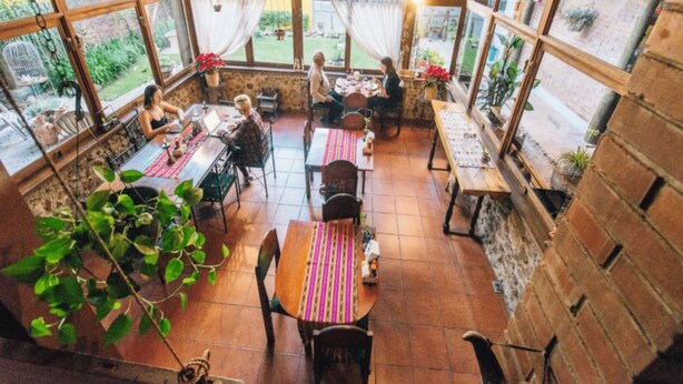 A spacious patio with multiple tables and chairs, large windows with curtains, and potted plants. - Dai Nonni Hotel (Guatemala City)