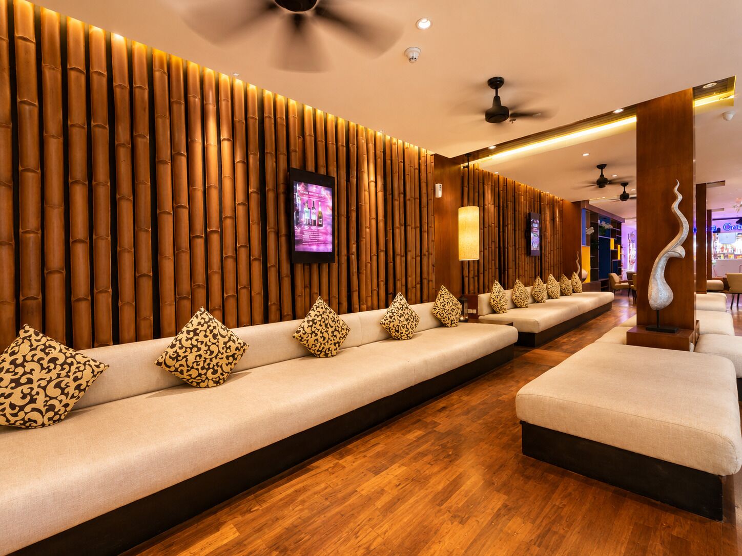 Hall d'albergo con una lunga reception, zona relax con cuscini decorati e una parete ornamentale con listelli di legno verticali.