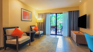 A hotel room with a sofa, armchair, TV, and a balcony with curtains.