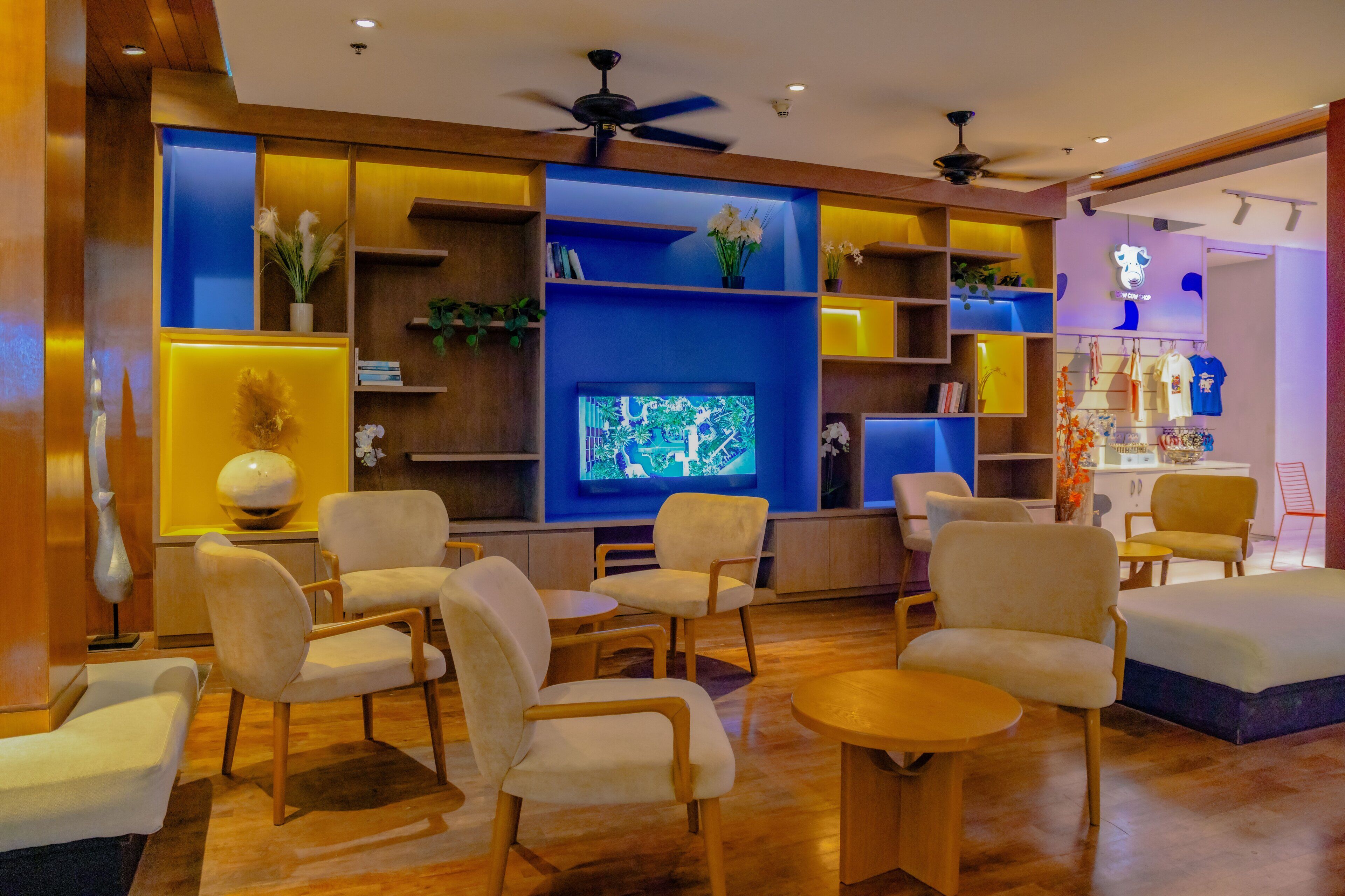 Un moderno vestíbulo de hotel con televisor, asientos cómodos y una variedad de plantas y decoraciones.