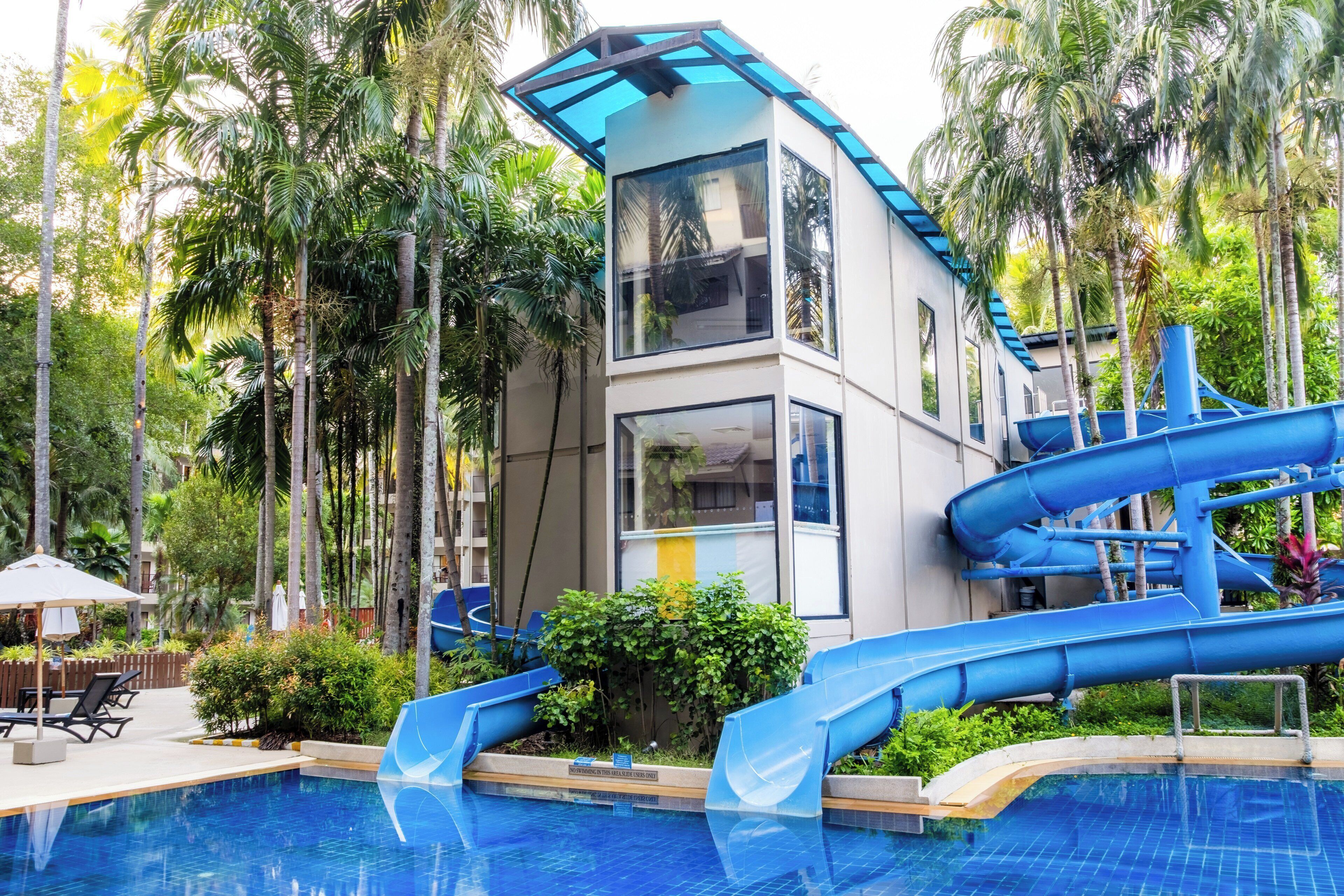 A modern building with a pool, slides, and lush greenery.