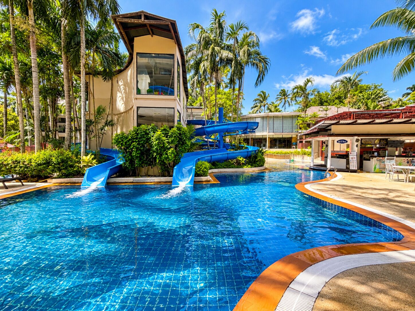Une piscine avec un toboggan, entourée de palmiers et bordée d’un bâtiment au design architectural unique.