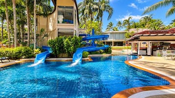 Une piscine avec un toboggan, entourée de palmiers et bordée d’un bâtiment au design architectural unique.