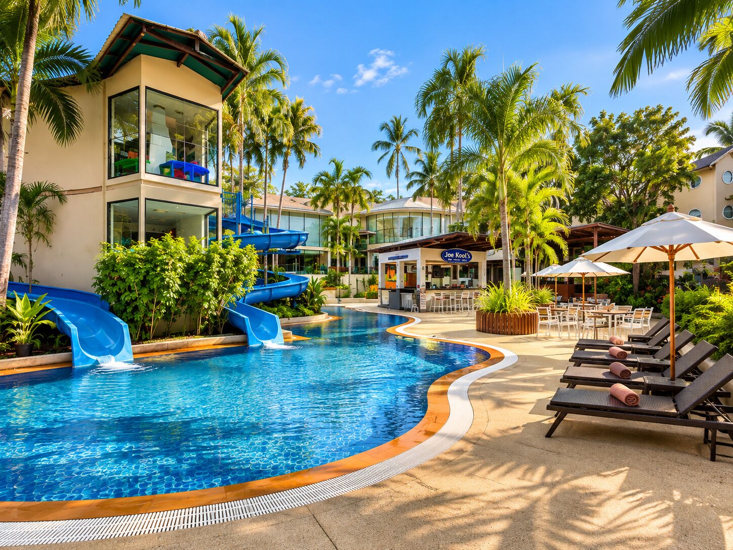 Une piscine de complexe hôtelier avec un toboggan bleu, des chaises longues et des palmiers.