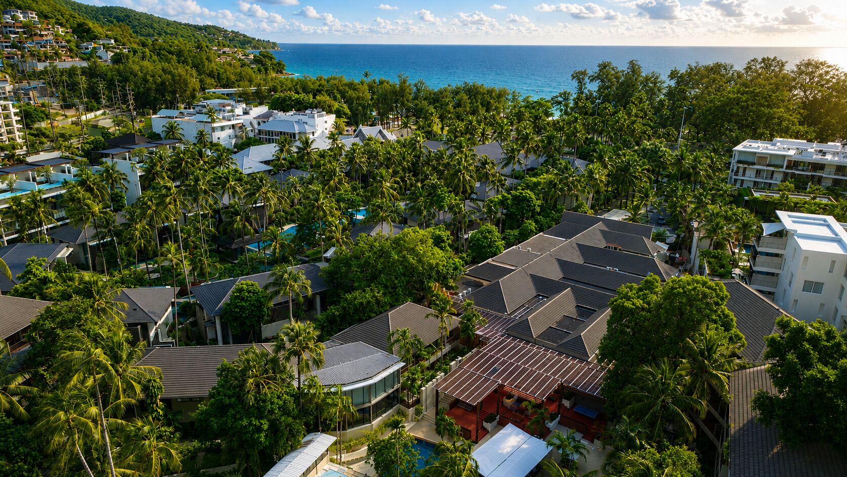 A coastal residential area with multiple buildings, some with sloped roofs, and dense greenery including palm trees.