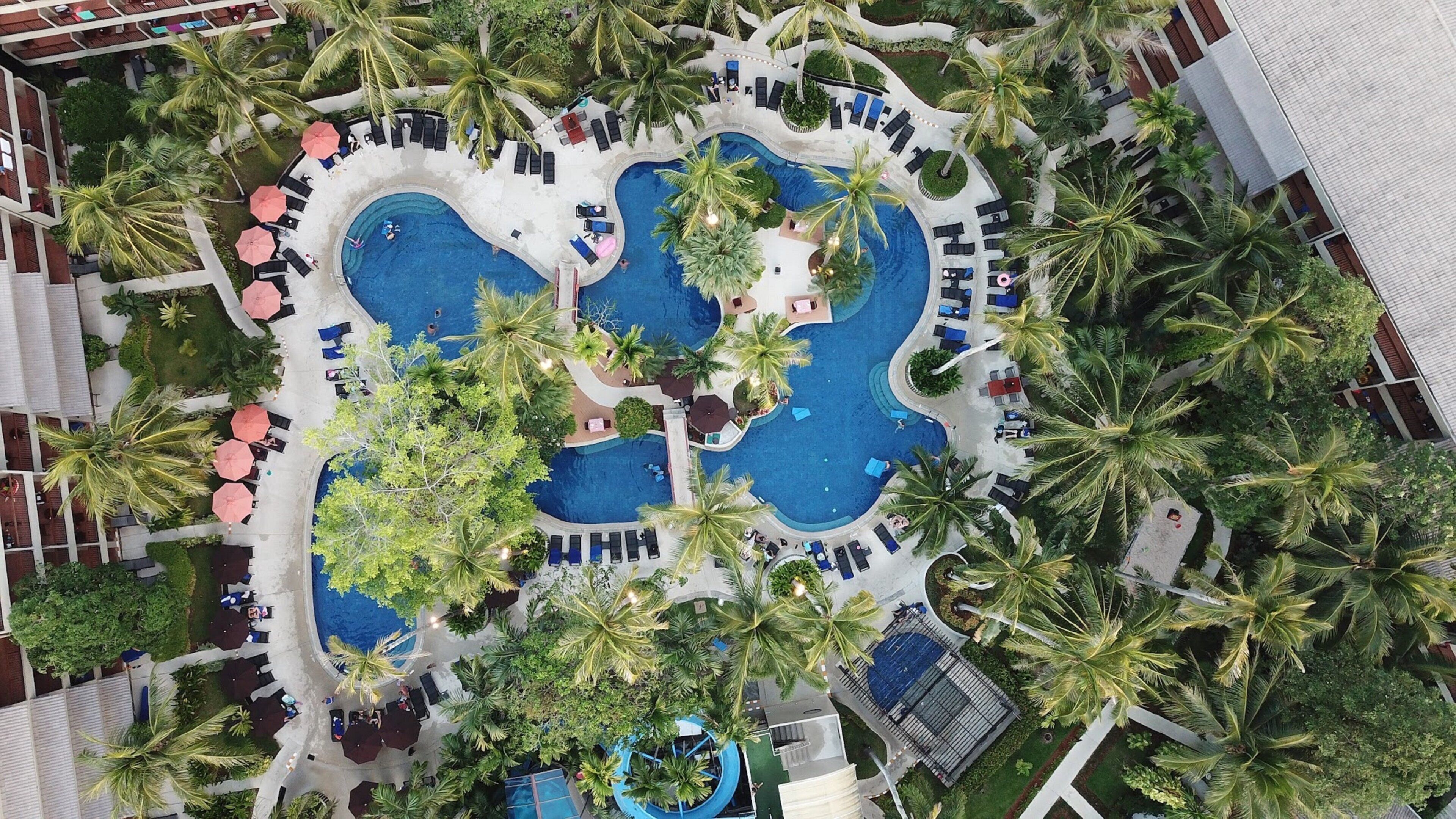 Vista aérea de un resort con varias piscinas, palmeras y zonas de descanso.