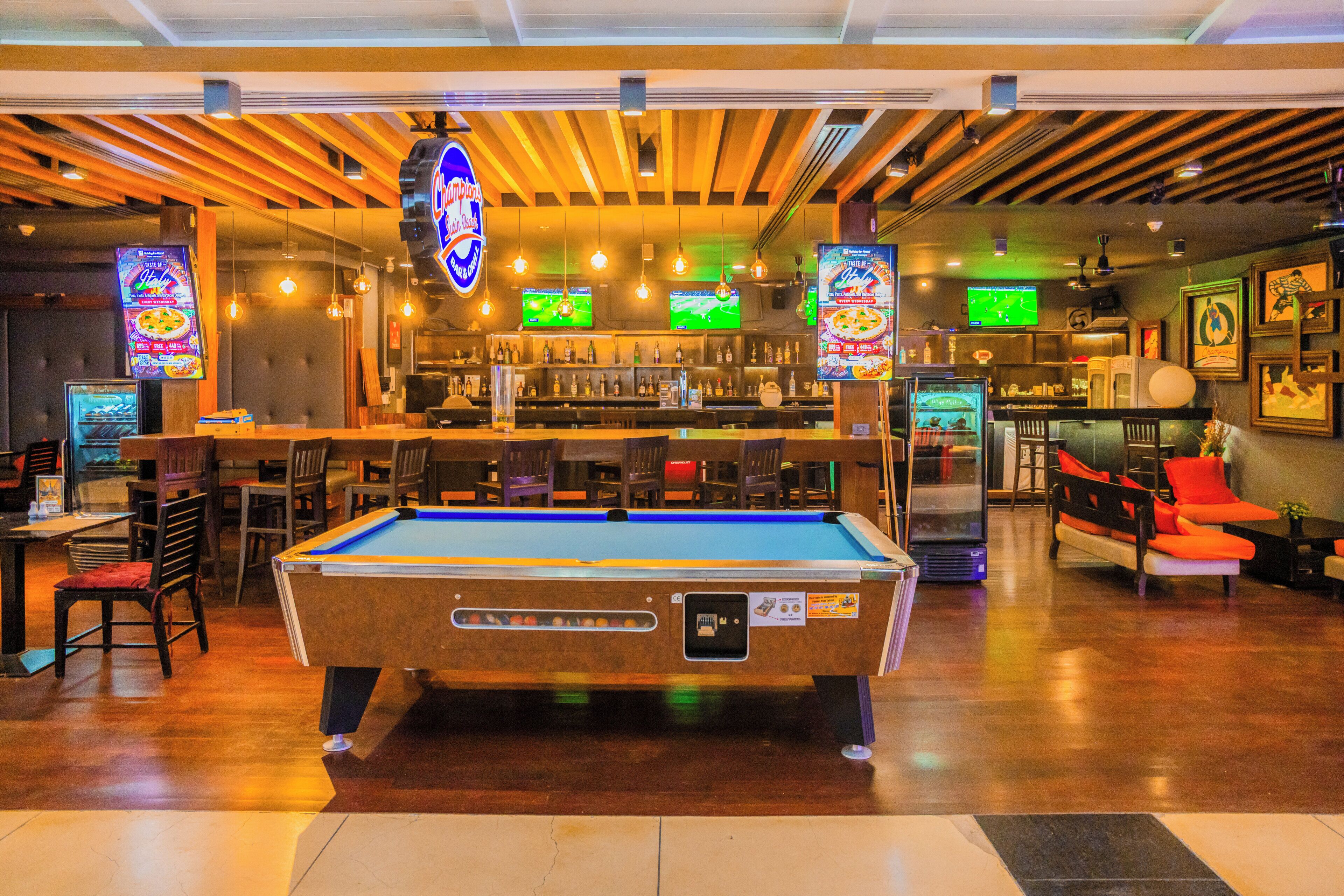 A pool table in a bar area with multiple screens displaying sports games.