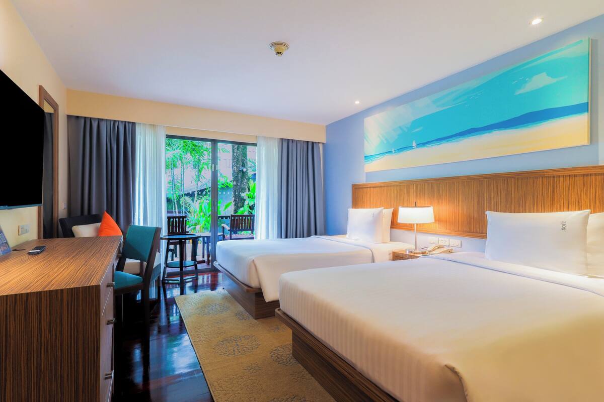 A hotel room with two beds, a desk, a chair, a TV, and a window with curtains.