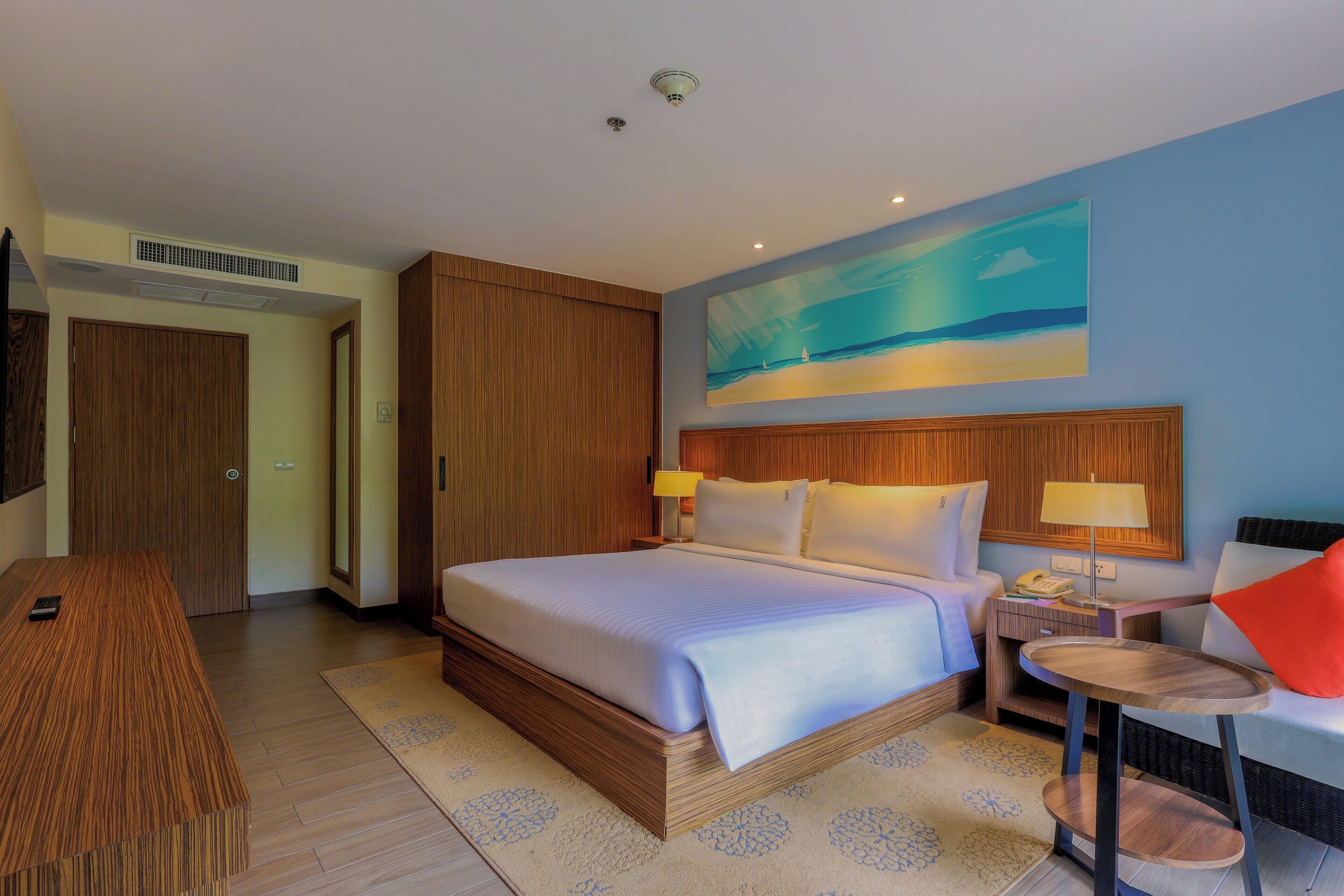 A hotel room with a large bed, a desk, a chair, and a painting on the wall.